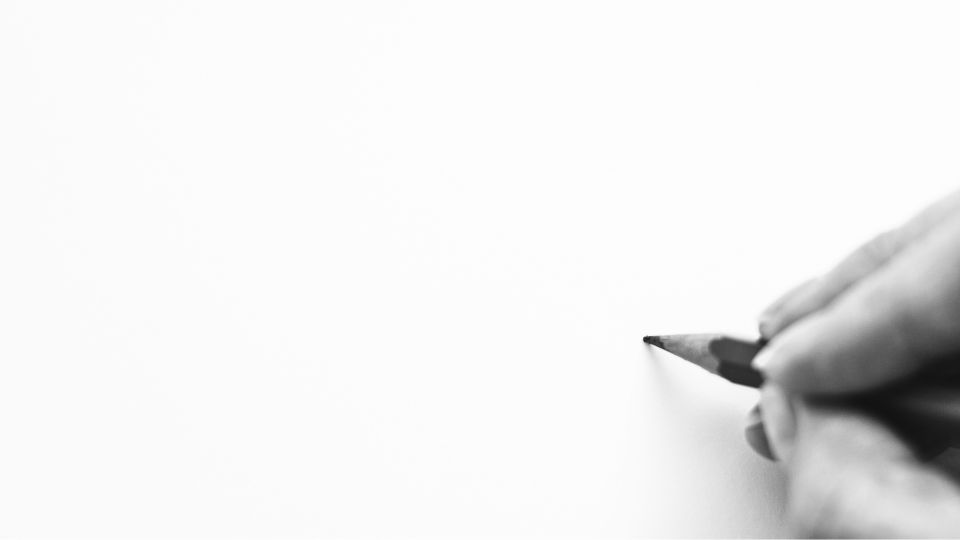 Uma mão segurando um lápis pronta para começar a desenhar num papel em branco.